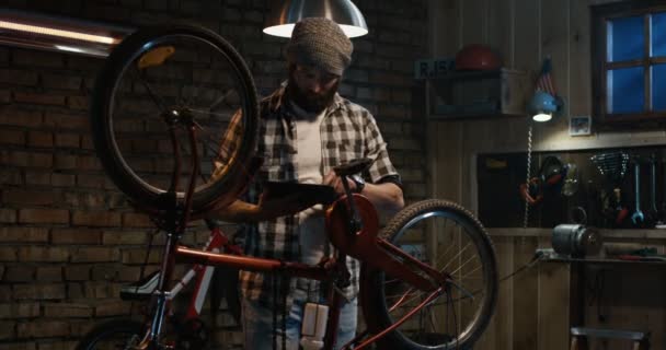 Hombre usando una tableta en un taller de reparación de bicicletas — Vídeos de Stock