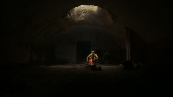 Jeune homme alimentant le feu dans la cabane souterraine — Video