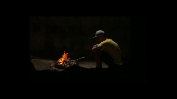 Junger Mann sitzt am Lagerfeuer — Stockvideo