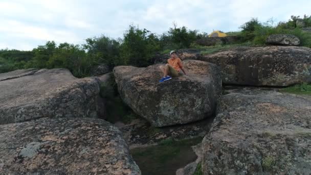 Молодий чоловік сидить на скелі — стокове відео