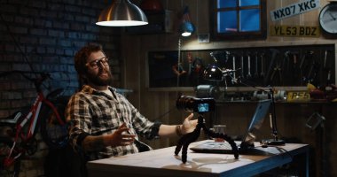 Genç adam bir atölyede fotoğraf makinesinde konuşuyor