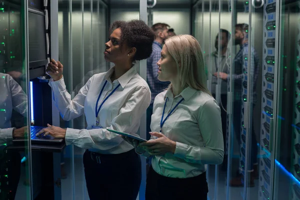 Dos mujeres están trabajando en un centro de datos con filas de bastidores de servidores — Foto de Stock