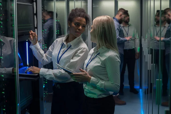 Dos mujeres están trabajando en un centro de datos con filas de bastidores de servidores — Foto de Stock