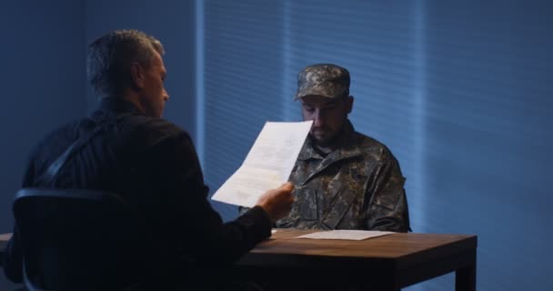 Експресивний поліцейський вивчає військового в кімнаті інтерв'ю — стокове відео
