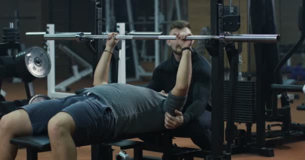 Treinador supervisionando jovem fazendo supino — Vídeo de Stock