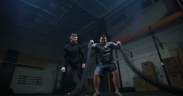 Trainer overseeing young man training with battle rope — Stock Video