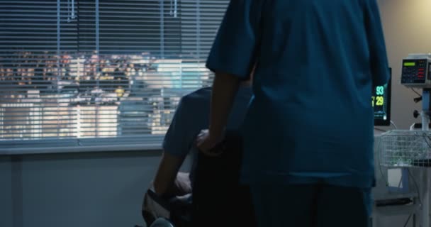 Медсестра толкает пациента с инвалидной коляской к окну — стоковое видео