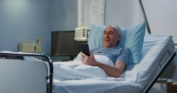 Чоловік пацієнт використовує відеодзвінок у лікарняній кімнаті — стокове фото