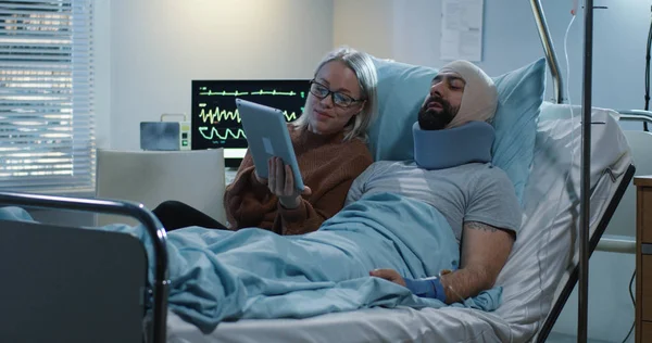 Yaralı adamla tablet kullanan bir kadın görülüyor.