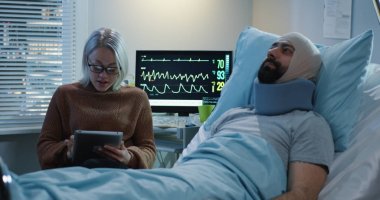 Yaralı adamla tablet kullanan bir kadın görülüyor.