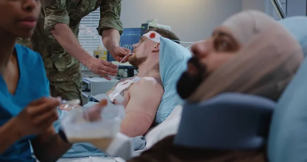 看護師は病院のベッドで負傷した兵士を養う — ストック写真