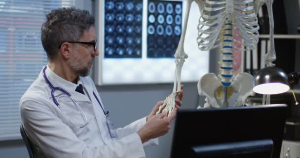 Médico usando o modelo de esqueleto para analisar a anatomia da mão — Vídeo de Stock