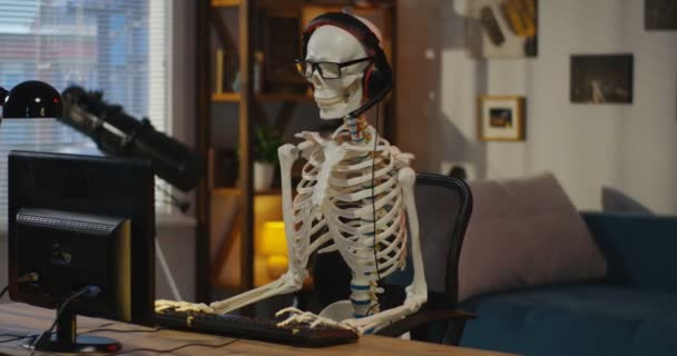 Скелет з навушниками, що сидять за комп'ютером — стокове відео