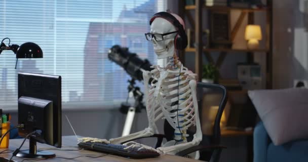 Skelet met koptelefoon zittend op computer — Stockvideo