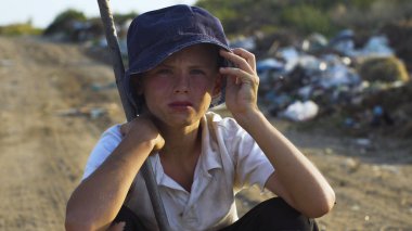 Kirli yüzlü çocuk çöplükte çömelmiş