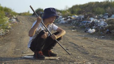 Kirli yüzlü çocuk çöplükte çömelmiş