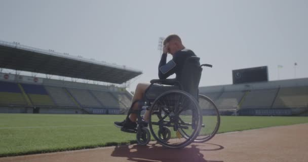 Disabled athlete sitting in wheelchair by a sports field — Stock Video