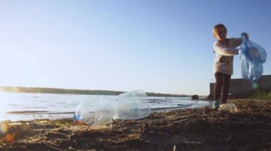 Girl collecting plastic bottles on riverbank