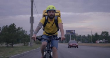 Bisikletli kurye yolda bisiklet sürüyor.