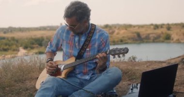 Adam çayırda elektro gitar çalıyor.
