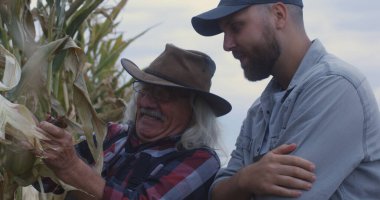 Neşeli yaşlı çiftçi torununa mısır gösteriyor.