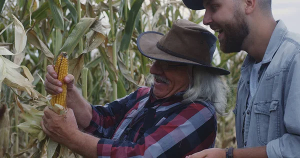 Neşeli yaşlı çiftçi torununa mısır gösteriyor.