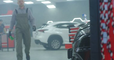 Erkek tamirci garajda yürüyor ve arabayı temizliyor.