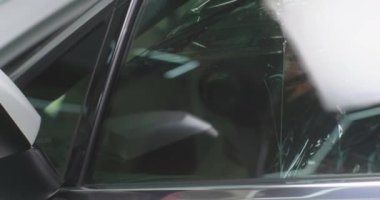 Erkek teknisyen arabanın camından film çıkarıyor.