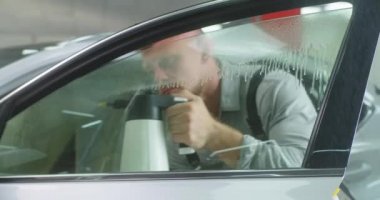 Erkek tamirci arabanın camını yıkıyor.