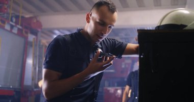 İtfaiyeci akıllı telefon kullanıyor ve iş arkadaşıyla konuşuyor.