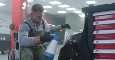 Tekerlekli sandalyedeki tamirci arabanın farına film uyguluyor.