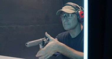 Olgun bir adam atış poligonunda tabanca ateşliyor.