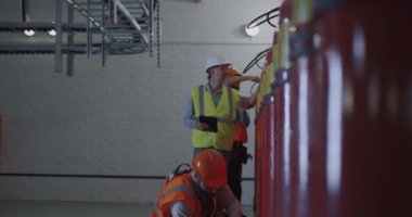 Olgun müfettiş yangın söndürücülerin yanındaki işçileri kontrol ediyor.