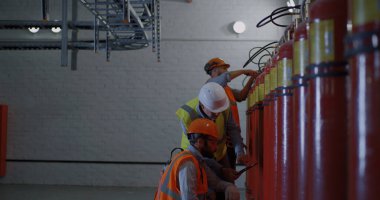 Olgun müfettiş yangın söndürücülerin yanındaki işçileri kontrol ediyor.