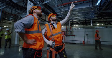 Fabrikada yürüyen ve konuşan erkek işçiler.