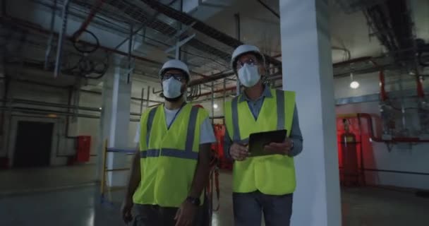 Инженеры в масках, изучающие металлические конструкции в цехе — стоковое видео