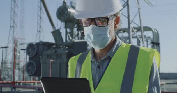 발전소에서 타블렛을 사용하는 마스크를 쓰고 있는 남자 기술자 — 비디오