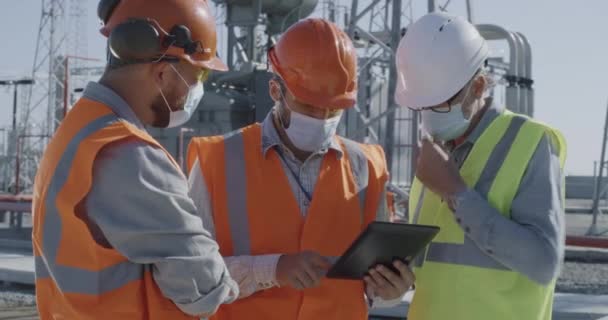 Los trabajadores masculinos en máscaras usando tableta juntos en la central eléctrica — Vídeos de Stock