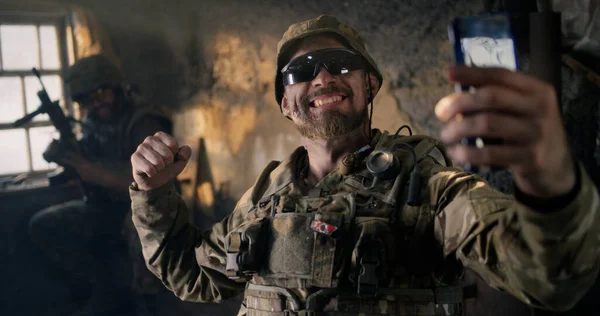 Katonai férfi okostelefont használ a piszkos épületben. — Stock Fotó