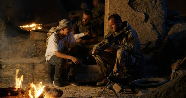 Kamp ateşi yakınında etnik gençlere silah gösteren bir asker — Stok fotoğraf