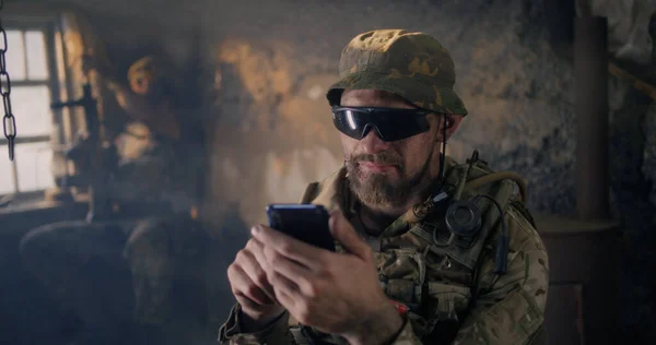 Military man using smartphone inside grungy building — Stock Photo, Image