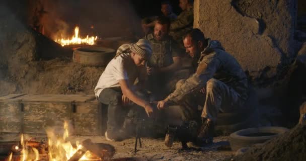 모닥불 근처에서 쉬고 있는 군인들과 십 대 청소년들 — 비디오