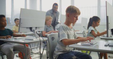 İlkokul öğrencileri bilgisayarlar üzerinde çalışıyor. Bilgisayar Bilimi Sınıfında Çeşitli Çocuklara Dijital Yetenek Uygulama ve Eğitim Programında Rehber Öğretmenlik. İnteraktif STEM Öğrenme. Doli Vuruşu.