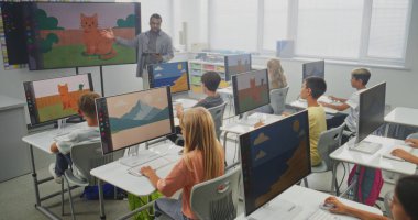 İlköğretim Okulu Çocukları Bilgisayar Kullanıyor, Dijital Resimler Oluşturuyor. Dijital ekranı kullanarak genç kızlara ve oğlanlara resim dersi veren Afrikalı Amerikalı öğretmen. BTMM Eğitim. Sabit Çekim.