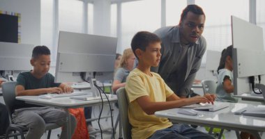 İlkokul öğrencileri bilgisayarlar üzerinde çalışıyor. Bilgisayar Bilimi Sınıfı 'nda Dijital Yetenekler Uygulamada ve Eğitim Programında Afrikalı Amerikalı Öğretmen Genç Çocuğa Rehber. Etkileşimli BTMM Öğrenme.