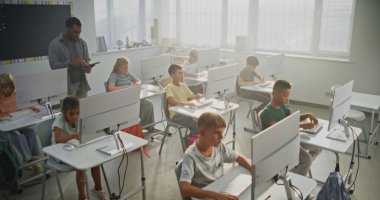 İlkokul öğrencileri bilgisayarlar üzerinde yaratıcı projeler üzerinde çalışıyorlar. Bilgisayar Bilimi dersi sırasında çeşitli çocuklara eğitim konusunda rehberlik eden Afro-Amerikan Öğretmen. Modern BTMM Öğrenme. Yüksek Açı