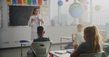 Beyaz önlüklü bayan doktor ziyaret sınıfında, İlkokul öğrencilerine sağlık ve hijyenle ilgili ders veriyor. Genç Çocuklar Oturuyor ve Dinliyor Profesyonel Sağlık Bakımına Cana Yakın.