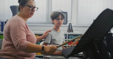 İlkokulda Perküsyon dersi sırasında Davul Çalan Yetenekli Çocuk, Ritim Duyusu Uygulaması. Genç Müzisyen Öğretmeni Davul Çalmayı Öğretiyor, Müzik Dersi Üzerine Notaları Açıklıyor.