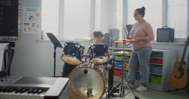 Modern Müzik Sınıfında Davul Çalışan İlkokul Çocuğu, Davulcu Olmanın Rüyası. Perküsyon Dersinde Davul Çalması için Yetenekli Çocuğu Eğiten Kadın Öğretmen. Ritim Eğitimi, Müzik Sanatı.