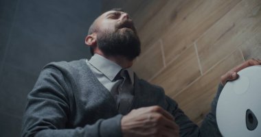 Tuvalette oturan ve tuvalette ishal ve mide acısından muzdarip bir adam. İş adamı Modern Ofis 'te Rahatsızlık, Hazımsızlık ve Sindirim Rahatsızlığı Yaşıyor. Düşük Açı.